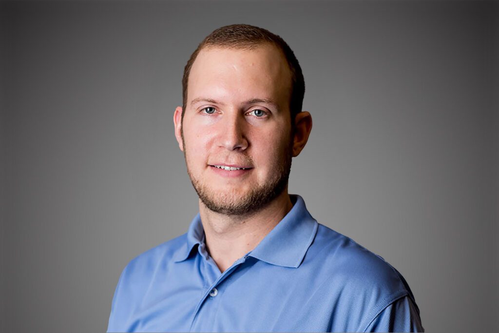 Headshot of Andrew Rous in front of a gray background.