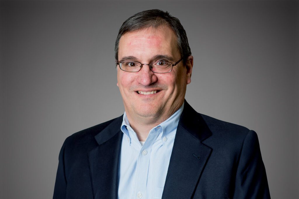 Headshot of Joe Oetter in front of a gray background.