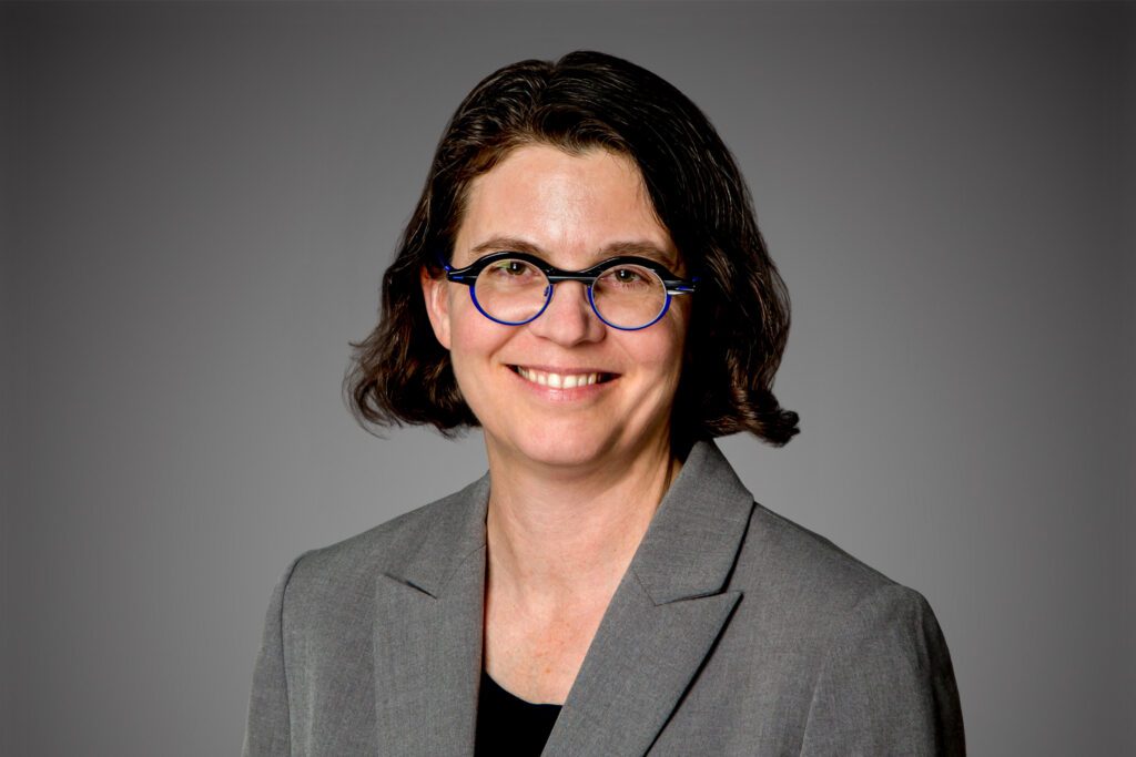 Headshot of Leigh McMillen in front of gray background.