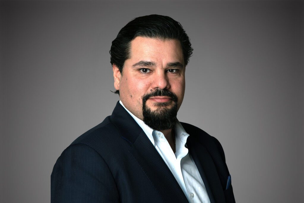 Headshot of Paul Rentzelos in front of a gray background.